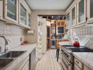 This charming kitchen features white tiled countertops and backsplash, complemented by cream-colored cabinetry with glass fronts.