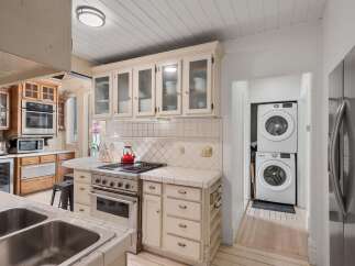 This kitchen features a stainless steel range with a red kettle, complemented by cream-colored cabinets and tiled countertops.