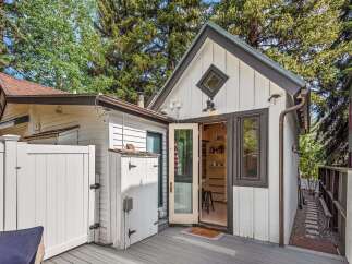Charming backyard oasis featuring a rustic white shed with black hardware and a diamond-shaped window, complemented by a spacious grey deck perfect for outdoor entertaining.