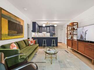 Experience modern living in this stylish open-concept space, featuring a vibrant green tufted sofa and a sleek navy blue kitchen with marble countertops.