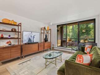 Experience modern living in this stylish living room, featuring a sleek entertainment center and a plush green sofa adorned with chic orange and white accent pillows.