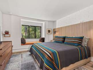 Experience ultimate comfort in this inviting bedroom, featuring a cozy window seat overlooking lush greenery.