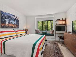 Experience mountain living in this cozy bedroom featuring a striking artwork of snow-capped peaks above a classic striped quilt.