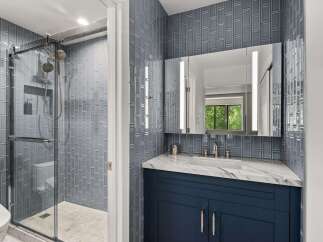 Experience modern luxury in this stunning bathroom featuring a sleek glass-enclosed shower with elegant gray subway tile and a spacious vanity with a marble countertop.