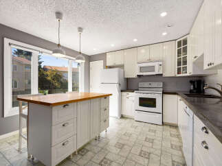 This spacious kitchen features white cabinetry, a large central island with a butcher block countertop, and a bright, airy feel.
