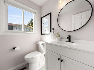 This modern bathroom features a sleek white vanity with black hardware, complemented by a black-framed round mirror and a stylish black faucet.