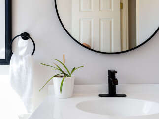 This modern bathroom features a sleek white vanity with a minimalist black faucet, complemented by a round black-framed mirror reflecting a clean interior.