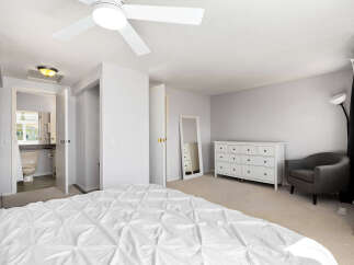 This spacious bedroom features a comfortable king-sized bed with a white duvet, a modern ceiling fan, and ample natural light.