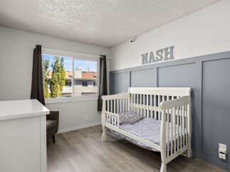 This charming nursery features a white crib with playful bedding, set against a stylish grey accent wall with decorative paneling.