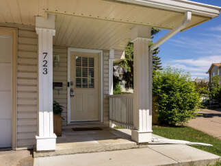 Welcome to this charming home featuring a covered front porch with a white railing and a beige front door.