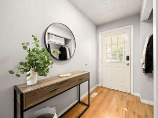 Welcome guests into this charming entryway featuring a sleek console table topped with a decorative vase and a round mirror reflecting the organized closet.