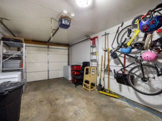 This garage offers ample storage solutions with a multi-tiered shelving unit and a large black trash bin.