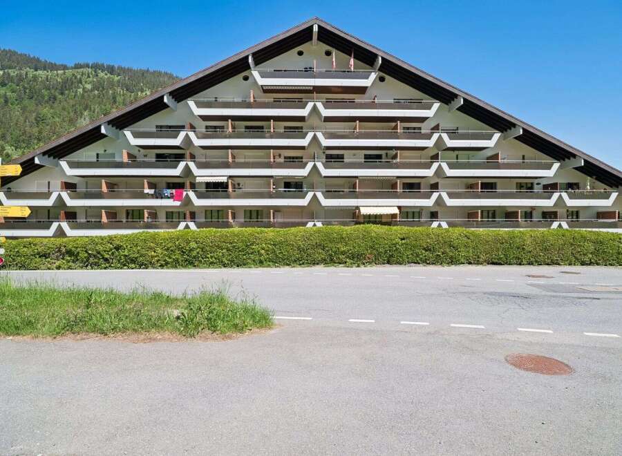 Discover this unique triangular apartment building nestled against a lush green hillside, offering stunning mountain views.