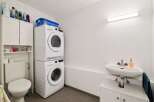 This modern laundry room features a stacked washer and dryer for space efficiency, complemented by a convenient toilet and a sleek sink with storage.