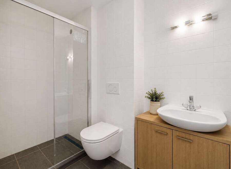 This modern bathroom features a sleek glass-enclosed shower and a wall-mounted toilet for a minimalist aesthetic.