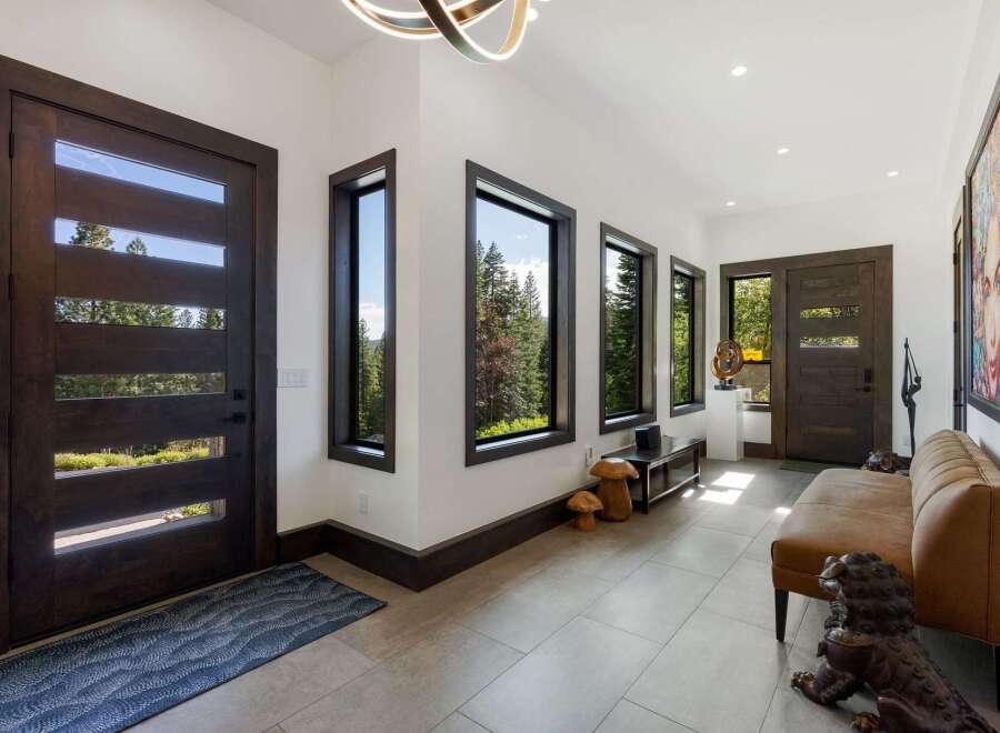 Step into this modern entryway featuring sleek, dark wood doors with horizontal glass panels that invite natural light and showcase stunning forest views.