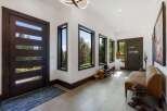 Step into this modern entryway featuring sleek, dark wood doors with horizontal glass panels that invite natural light and showcase stunning forest views.