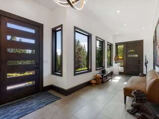 Step into this modern entryway featuring sleek, dark wood doors with horizontal glass panels that invite natural light and showcase stunning forest views.