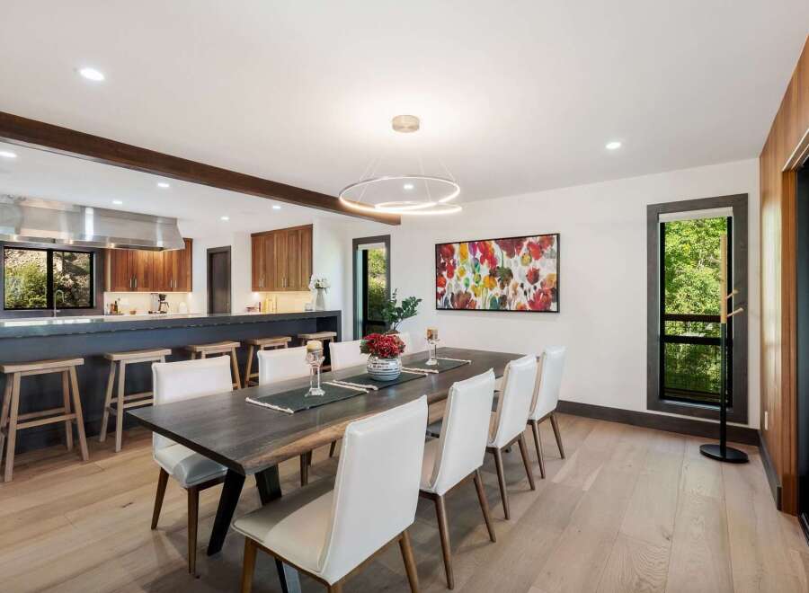 Experience modern living in this stunning dining area, featuring a spacious dark wood table complemented by elegant white chairs.