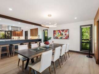 Experience modern living in this stunning dining area, featuring a spacious dark wood table complemented by elegant white chairs.