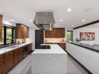 Experience luxury in this modern kitchen featuring sleek walnut cabinetry and a spacious quartz island with a built-in gas range.