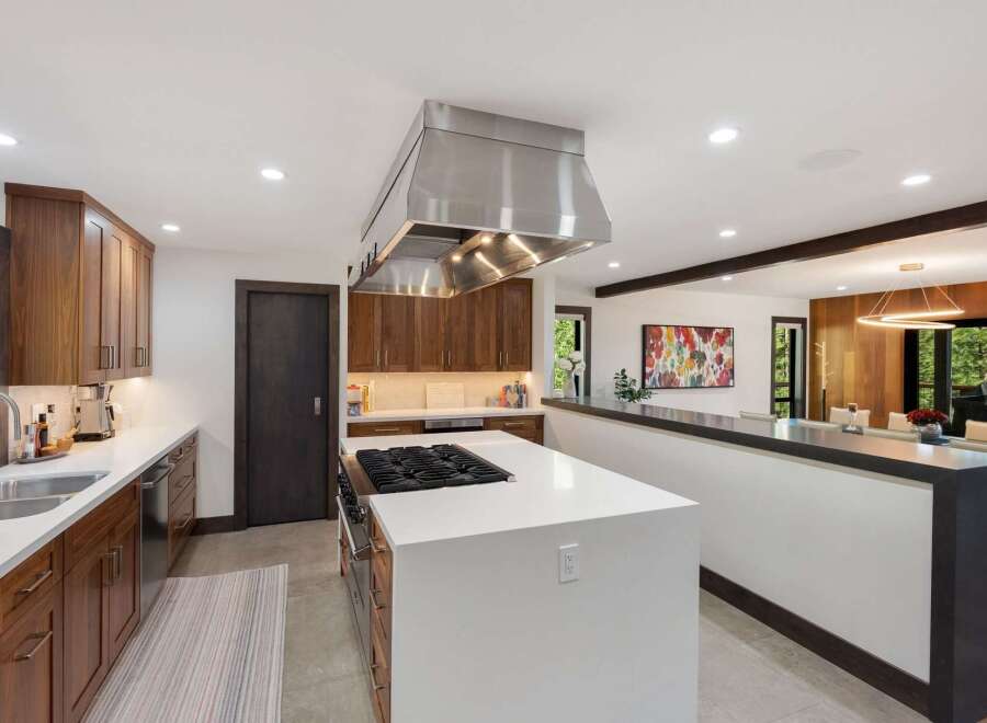 Experience luxury in this modern kitchen featuring sleek, dark wood cabinetry and a spacious white island with a built-in gas range.