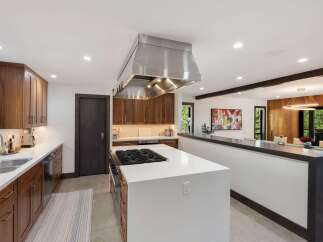Experience luxury in this modern kitchen featuring sleek, dark wood cabinetry and a spacious white island with a built-in gas range.