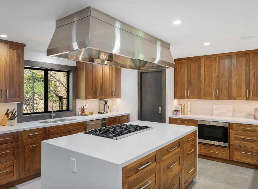 Experience luxury in this modern kitchen featuring rich walnut cabinetry and a sleek stainless steel range hood.