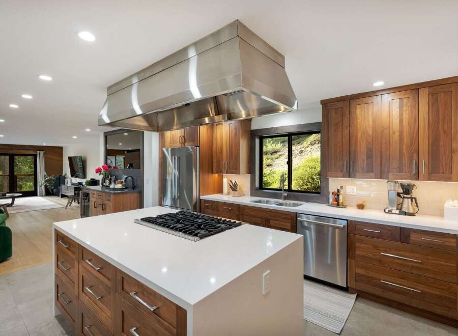 Experience luxury living in this stunning modern kitchen, featuring rich walnut cabinetry and a sleek white quartz island with a built-in gas range.