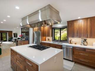 Experience luxury living in this stunning modern kitchen, featuring rich walnut cabinetry and a sleek white quartz island with a built-in gas range.