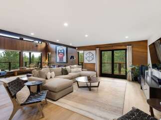 Experience luxurious living in this stunning modern home, featuring a spacious open-concept living area with floor-to-ceiling wood paneling and expansive windows that offer breathtaking forest views.