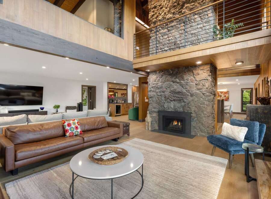 Experience luxury living in this stunning great room, featuring a dramatic floor-to-ceiling stone fireplace and a soaring vaulted ceiling with exposed beams.
