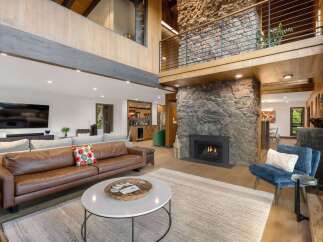 Experience luxury living in this stunning great room, featuring a dramatic floor-to-ceiling stone fireplace and a soaring vaulted ceiling with exposed beams.
