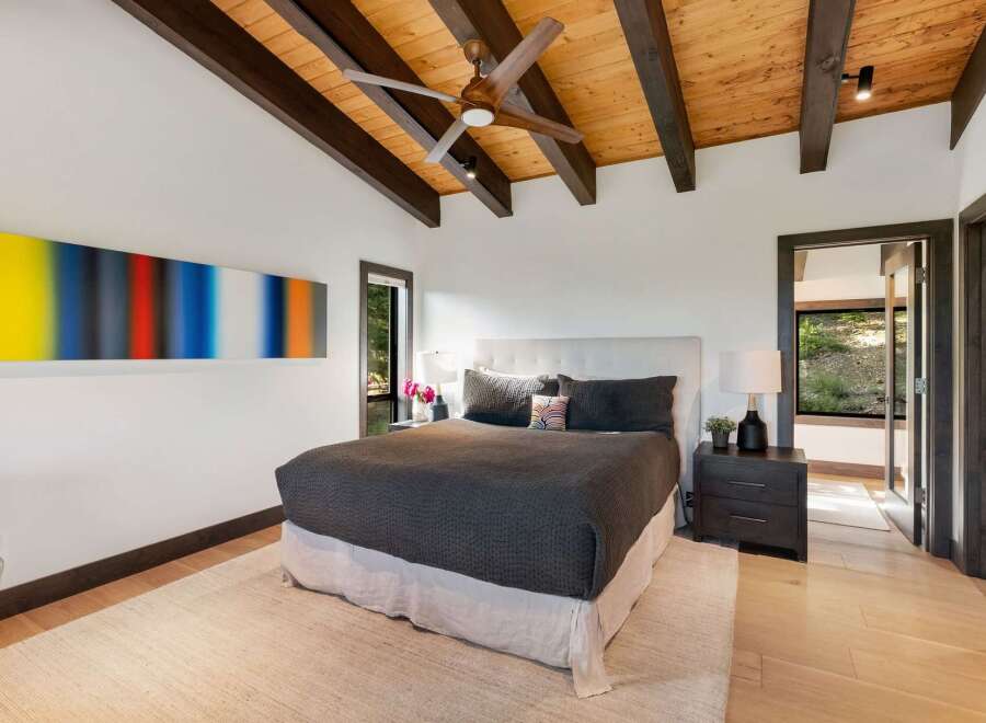Experience modern luxury in this stunning bedroom, featuring a vaulted wood-beamed ceiling and a striking abstract art piece.