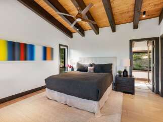 Experience modern luxury in this stunning bedroom, featuring a vaulted wood-beamed ceiling and a striking abstract art piece.