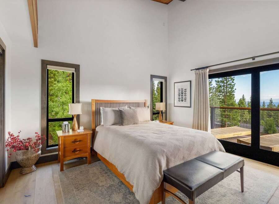Experience serene mountain living in this beautifully appointed bedroom, featuring a spacious king-sized bed and large windows that frame breathtaking forest and lake views.