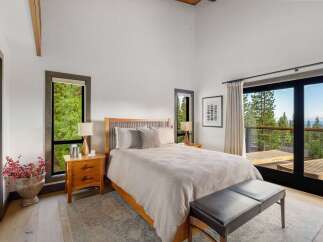 Experience serene mountain living in this beautifully appointed bedroom, featuring a spacious king-sized bed and large windows that frame breathtaking forest and lake views.