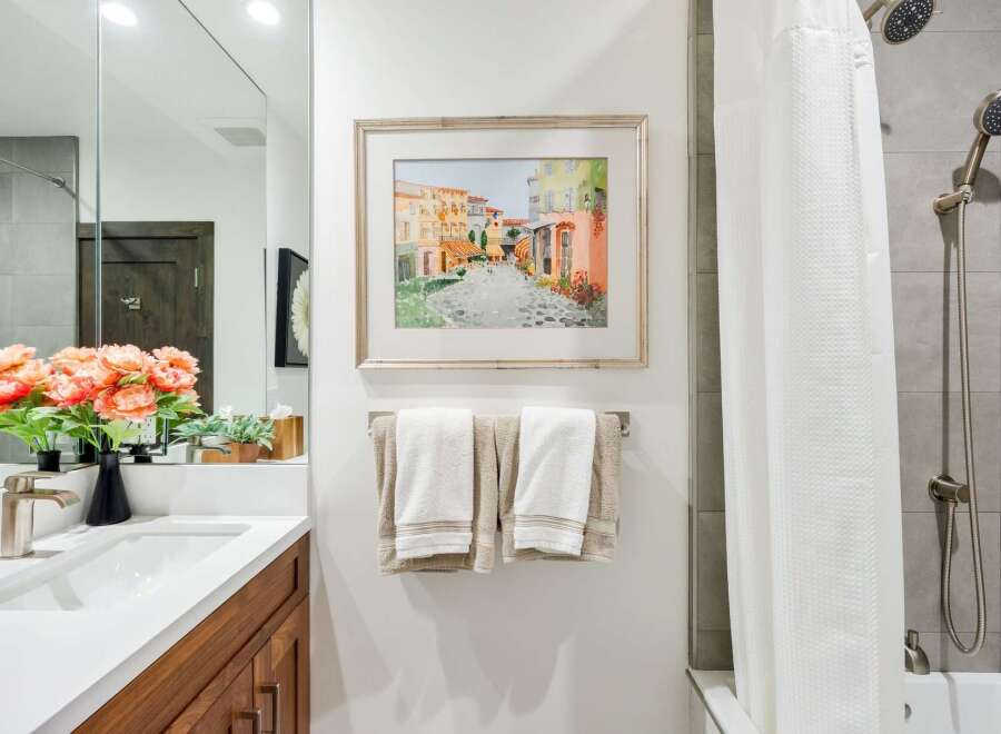 This modern bathroom features a sleek vanity with a white countertop and wooden cabinetry, complemented by a large mirror and vibrant floral arrangements.