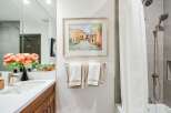 This modern bathroom features a sleek vanity with a white countertop and wooden cabinetry, complemented by a large mirror and vibrant floral arrangements.