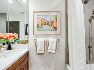 This modern bathroom features a sleek vanity with a white countertop and wooden cabinetry, complemented by a large mirror and vibrant floral arrangements.