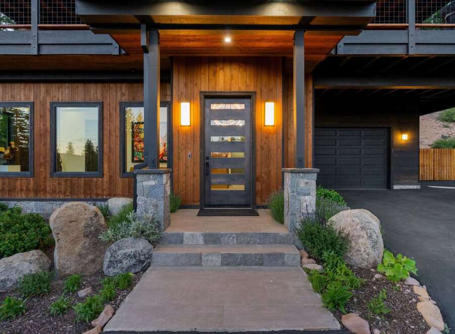 Experience modern mountain living in this stunning home, featuring a striking wood exterior and a sleek glass-paneled front door.