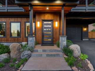 Experience modern mountain living in this stunning home, featuring a striking wood exterior and a sleek glass-paneled front door.