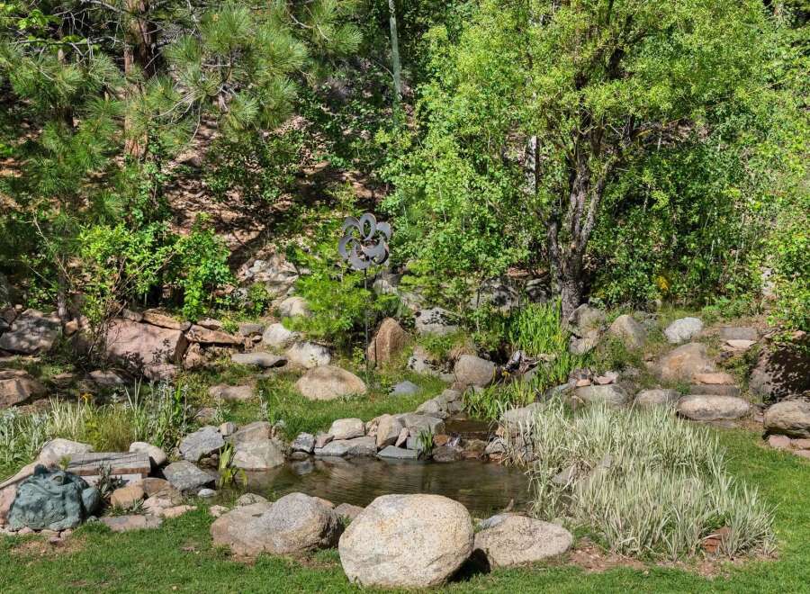 Discover a serene backyard oasis featuring a charming water feature surrounded by lush greenery and natural rock landscaping.