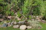 Discover a serene backyard oasis featuring a charming water feature surrounded by lush greenery and natural rock landscaping.