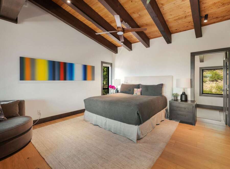 Experience modern mountain living in this stunning bedroom featuring a vaulted wood-beamed ceiling and a striking abstract art piece.