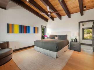 Experience modern mountain living in this stunning bedroom featuring a vaulted wood-beamed ceiling and a striking abstract art piece.