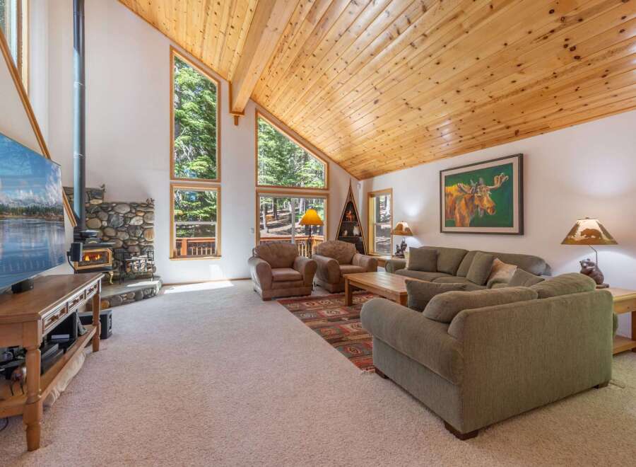 Experience rustic charm in this spacious living room, featuring a stunning stone fireplace and a soaring wood-paneled vaulted ceiling.
