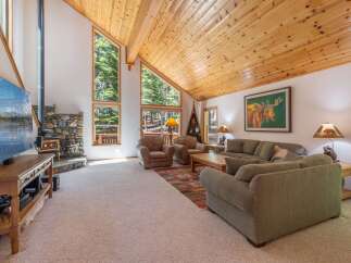 Experience rustic charm in this spacious living room, featuring a stunning stone fireplace and a soaring wood-paneled vaulted ceiling.