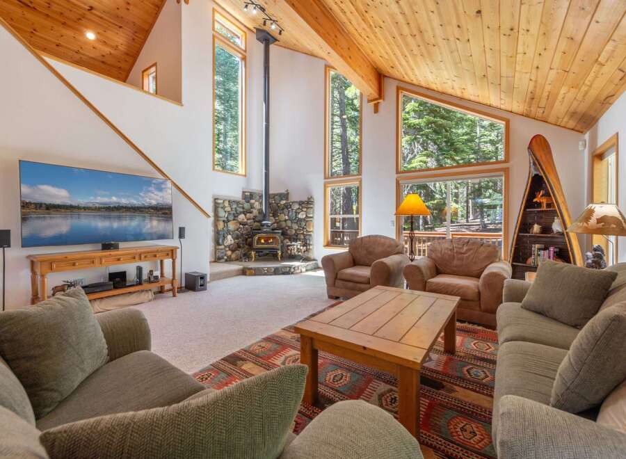 Experience rustic charm in this spacious living room, featuring a striking stone fireplace and a soaring wood-paneled ceiling.