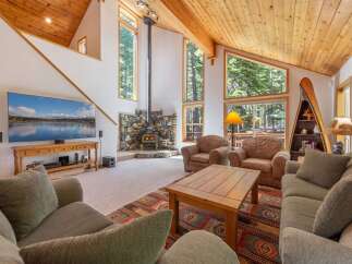 Experience rustic charm in this spacious living room, featuring a striking stone fireplace and a soaring wood-paneled ceiling.